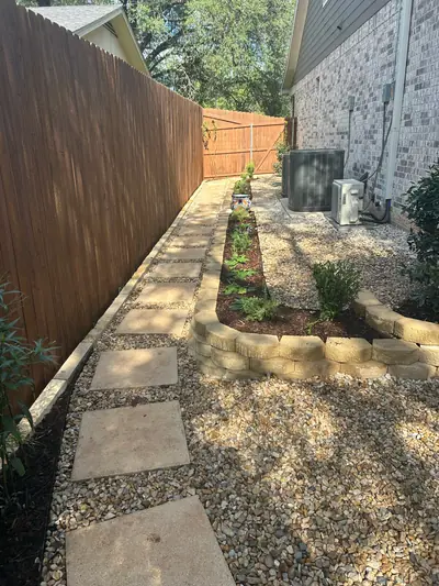 After: square stepping stones in gravel beside a planted border between the house and wooden fence.