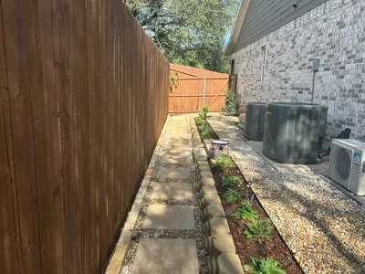 After: a stone path, low planted border, and gravel around air conditioning units beside the house.