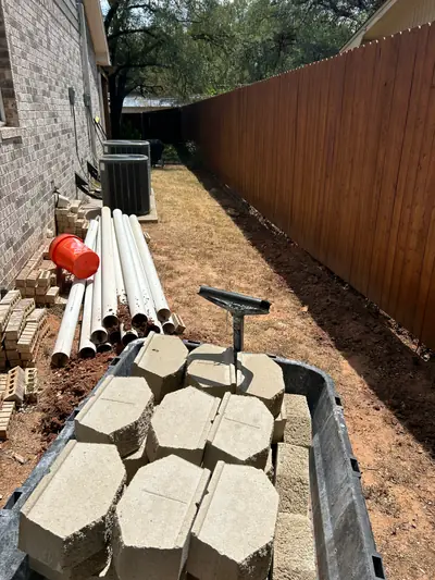 Before: the narrow side yard between the brick house and wooden fence, with materials awaiting work.